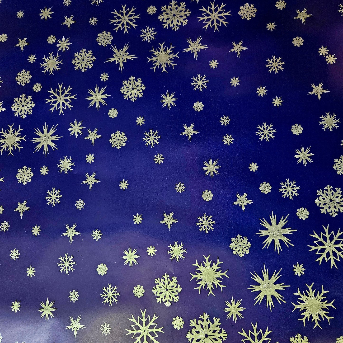 A close-up view of a blue Christmas wrapping paper with a dense pattern of silver snowflake designs.