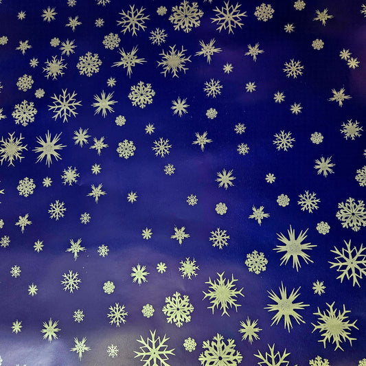A close-up view of a blue Christmas wrapping paper with a dense pattern of silver snowflake designs.