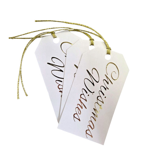 White gift tags with gold foil text Christmas wishes and lurex string on a white background.
