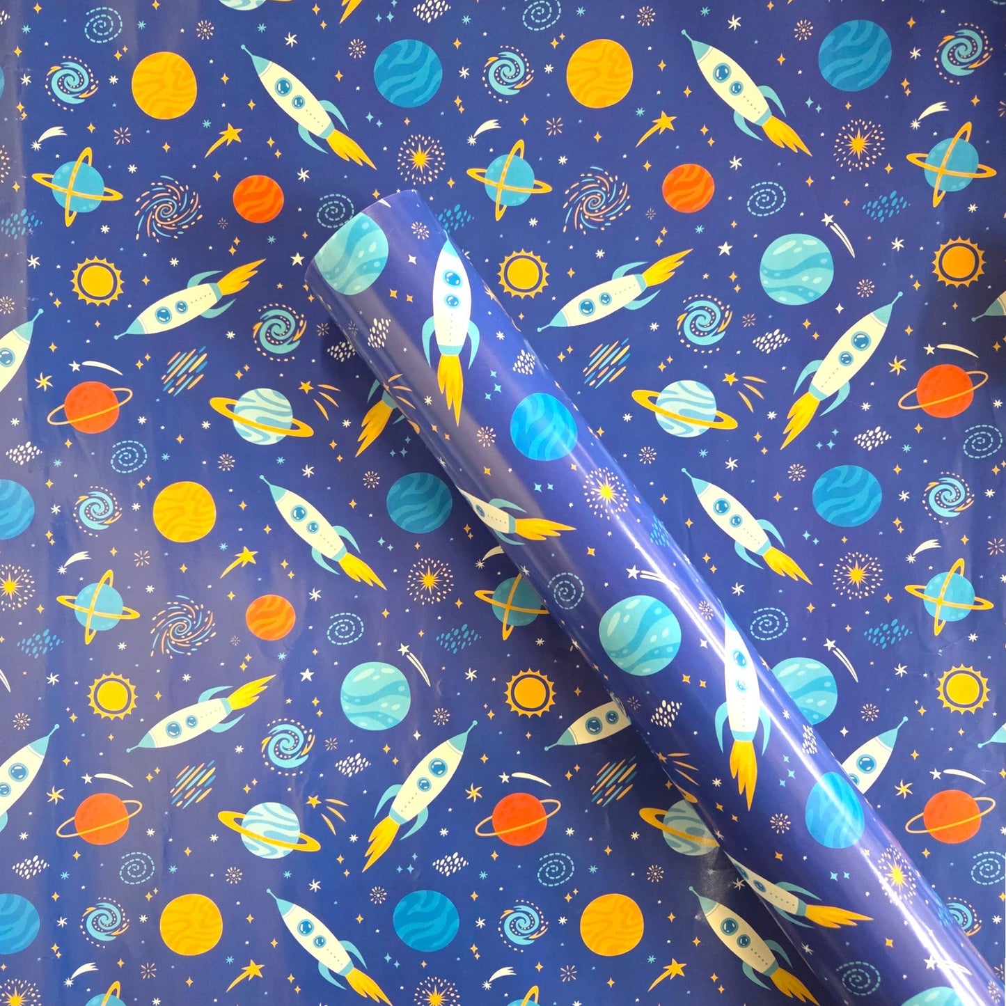 Space-themed wrapping paper with rockets, planets, and stars on a blue background.