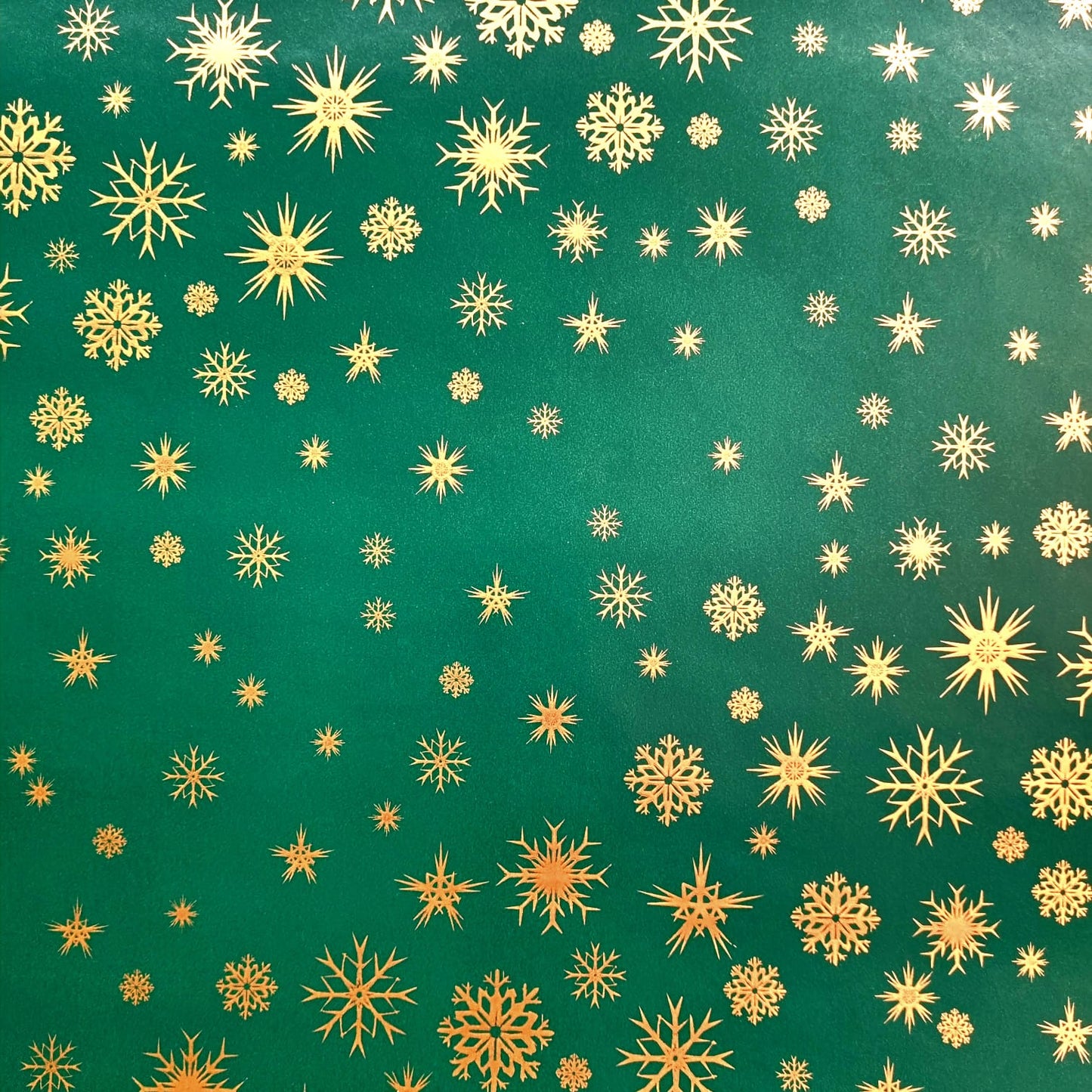 A roll of green wrapping paper with a pattern of small gold snowflakes.